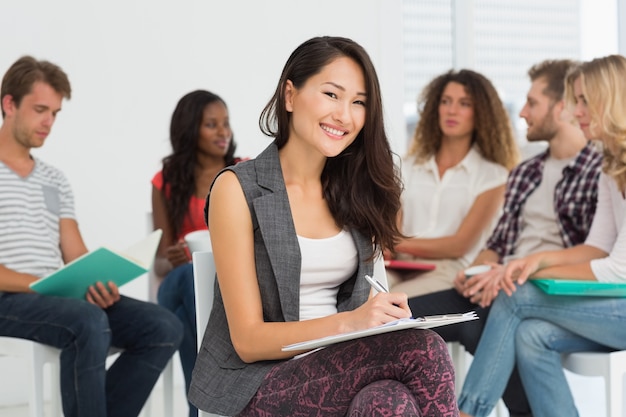 Smiling woman taking notes while colleagues are talking behind her