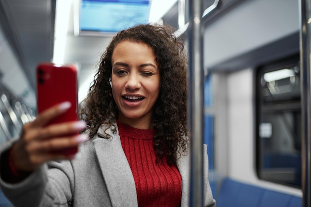 Smiling woman taking a selfie while standing on a subway train