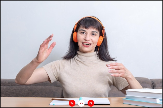 Smiling woman teacher in headphones explains the lesson viewing the screen of a video calling Online learning concept