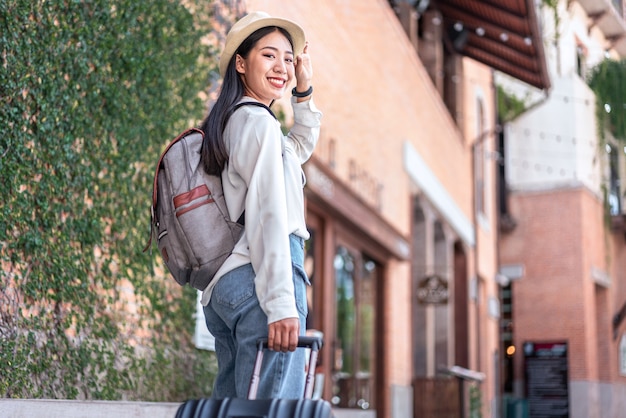 Smiling woman traveller dragging black suitcase luggage bag walking to passenger boarding in airport, Travel concept.