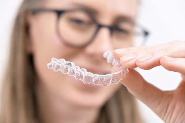 Smiling woman using clear plastic removable braces aligner or whitening tray dental orthodontic care