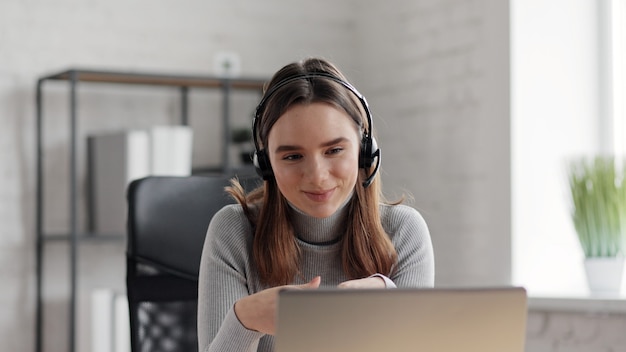 Smiling woman using laptop and wireless headset for online meeting, video call, video conference.