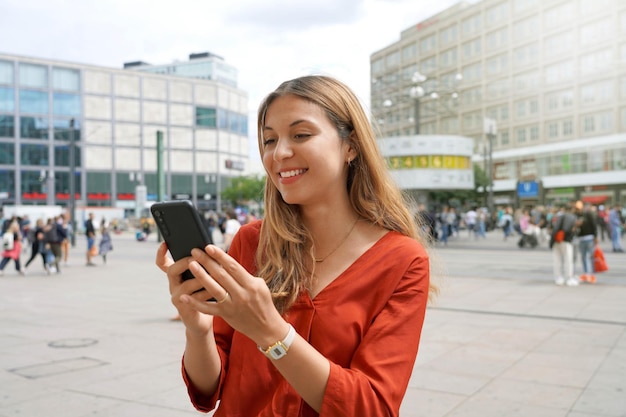 Smiling woman using smartphone in Alexanderplatz square in Berlin Germany