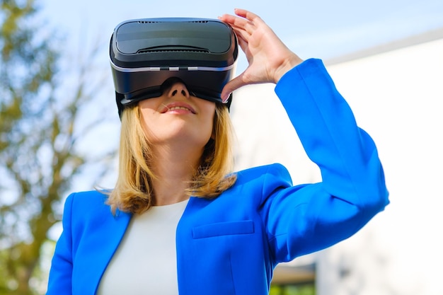 Smiling woman in vr glasses experiencing augmented reality in front of a business center futuristic