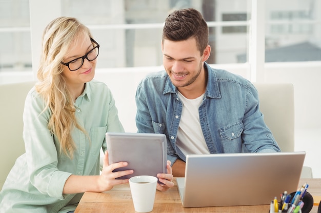 Smiling woman wearing eyeglasses showing digital tablet to man 