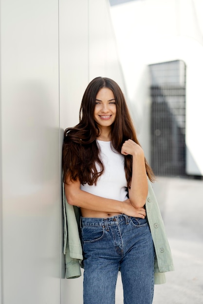 Smiling woman with beautiful long hair wearing jeans, tank top looking at camera on urban street