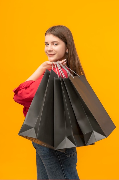 Smiling woman with big black shopping bags Bright yellow background Woman smiles after good shopping Vertical frame