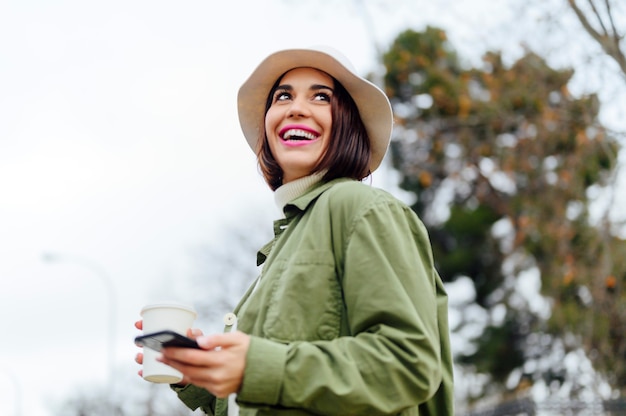 Smiling woman with coffee and smartphone on the street