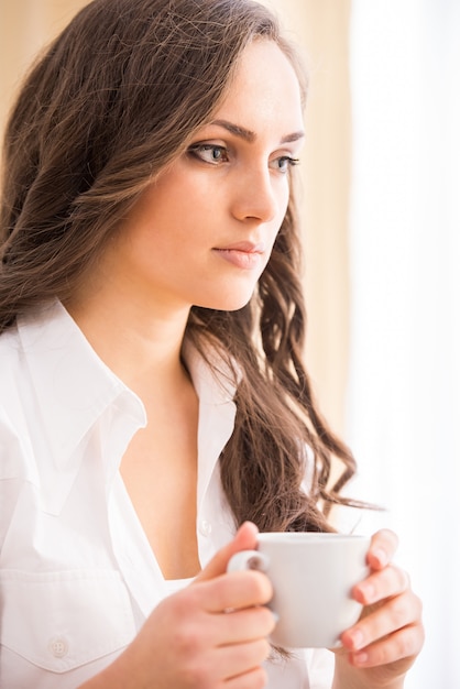 Smiling woman with coffee on sofa is looking at camera.