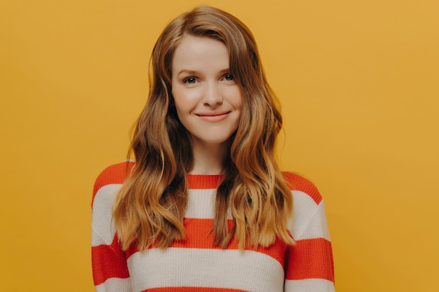 Smiling woman with flowing hair wearing a striped sweater her contented expression a burst of warmth against a yellow backdrop