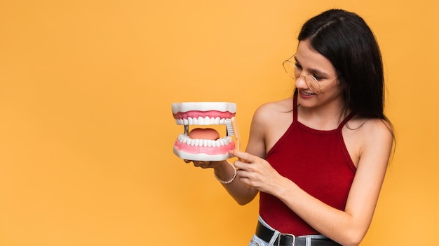 A smiling woman with healthy teeth cleans the shape of the jaws with a toothbrush on a yellow background Oral hygiene A place for your text