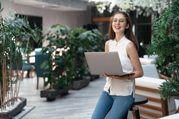 Smiling woman with a laptop standing in an empty cafe hall