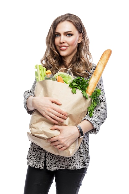 Smiling woman with paper bag with groceries A beautiful blonde woman is holding a bag with vegetables fruit and baguette Isolated on white background Vertical