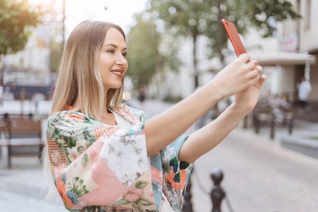 Smiling woman with a smartphone taking a selfie on a city street