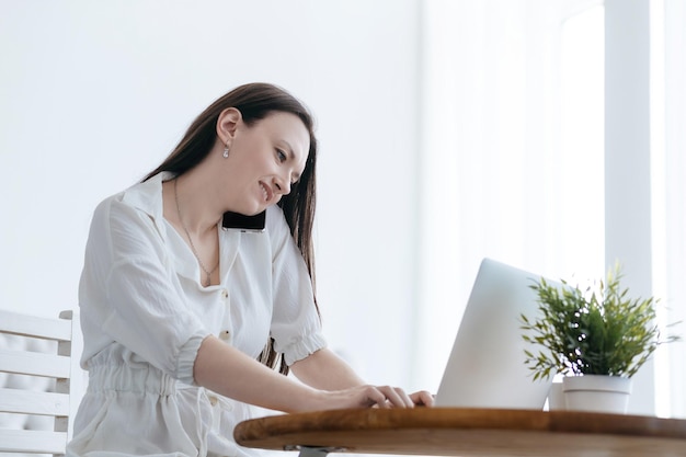 Smiling woman working on a laptop and talking on her smartphone