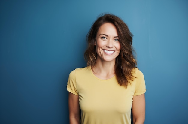 Photo smiling woman in a yellow shirt standing against a blue wall looking confident and happy with