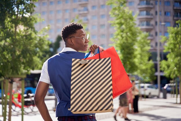 Smiling young african american man carrying shopping bags and looking at camera