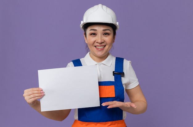 Smiling young asian builder girl with white safety helmet holding paper sheet