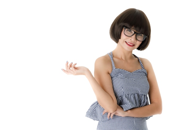 Smiling young Asian female model in checkered outfit and trendy eyeglasses looking at camera and using hand and finger pose in advertising gesture on white background.