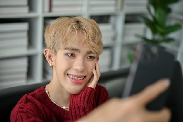 A smiling young Asian gay man is taking selfies through his smartphone