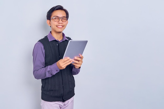 Smiling young Asian man in casual shirt and vest using tablet pc computer isolated on white background People lifestyle concept