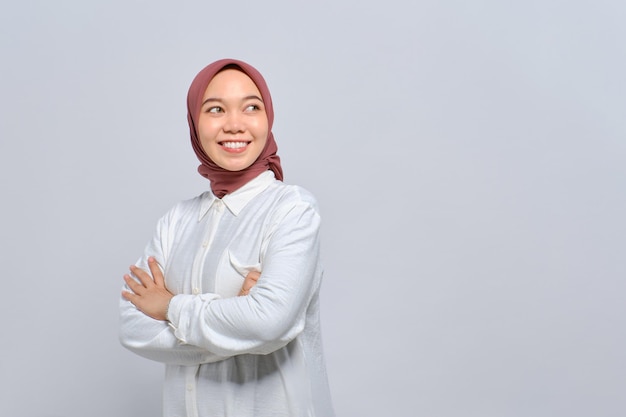 Smiling young Asian Muslim woman with arms crossed and looking away to copy space isolated over white background