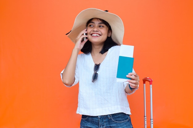 Smiling young Asian traveler holding boarding pass passport ticket and talking on smartphone