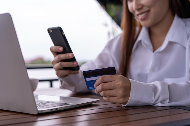 The smiling young Asian woman enjoys shopping online via a smartphone and paying online via credit card Convenience of spending without cash stay safe shopping from home and Social distance