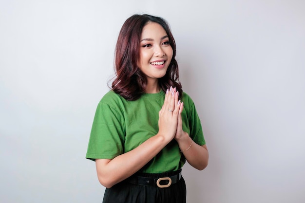 Smiling young Asian woman gesturing traditional greeting isolated over white background