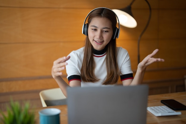 Smiling young asian woman in headset wave greet talking on webcam virtual conversation on laptop happy female in wireless headphones speak on video call on computer consult client online