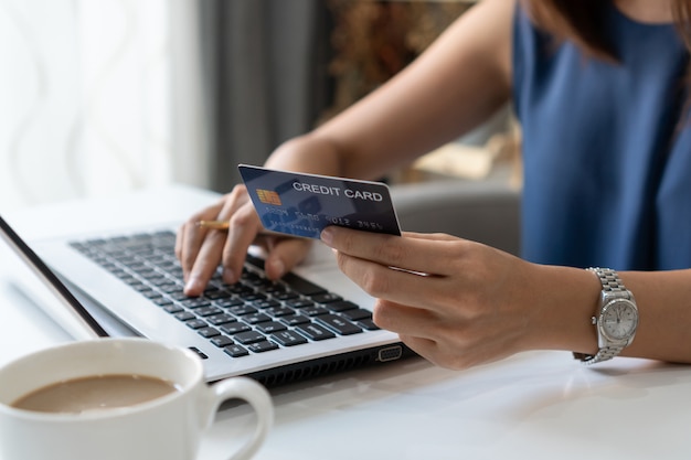 Smiling young Asian woman holding credit card while using computer laptop at home office