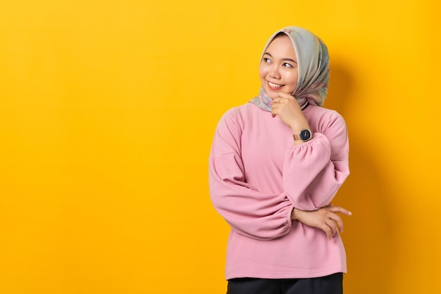 Smiling young Asian woman in pink shirt looking away at copy space on yellow background