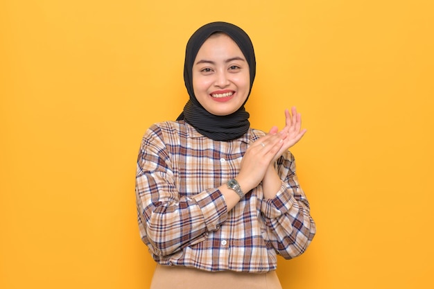 Smiling young Asian woman in plaid shirt clapping hands celebrating success congratulating someone isolated on yellow background