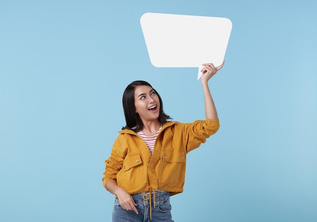 Smiling young Asian woman showing empty speech bubble in blue studio background