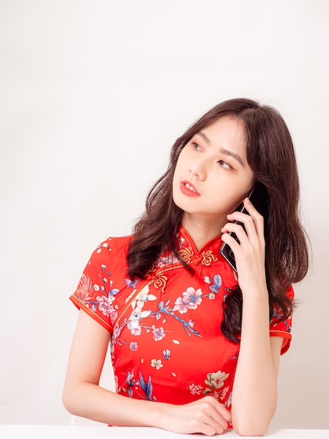 Smiling young asian woman in traditional cheongsam qipao dress talking on cellphone isolated on white background