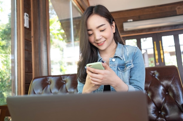 Smiling young Asian woman using smartphone at coffee shop Working online technology system concept