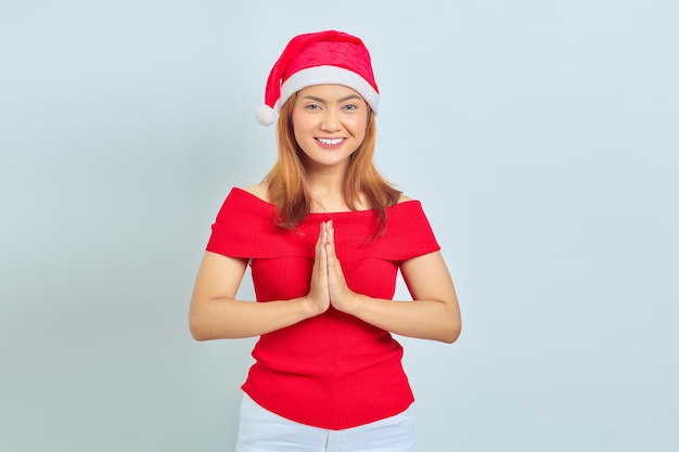 Smiling young Asian woman with Christmas hat holding hands and feeling optimistic