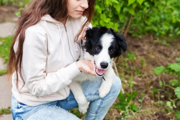 Smiling young attractive woman embracing huging cute puppy dog border collie in summer city park outdoor background