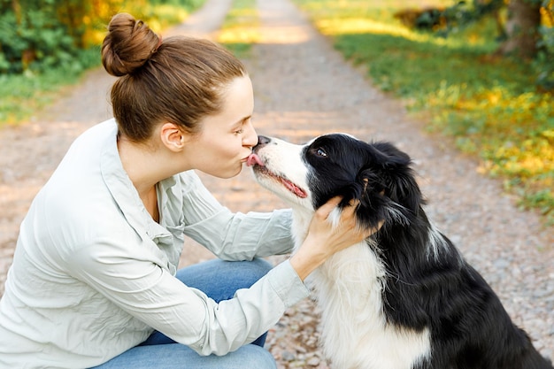 Smiling young attractive woman playing with cute puppy dog border collie on summer outdoor backgroun