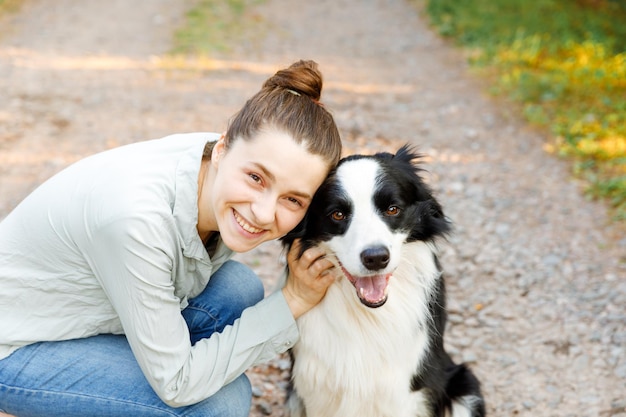 Smiling young attractive woman playing with cute puppy dog border collie on summer outdoor backgroun...