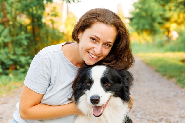 Smiling young attractive woman playing with cute puppy dog border collie on summer outdoor background Girl holding embracing hugging dog friend Pet care and animals concept