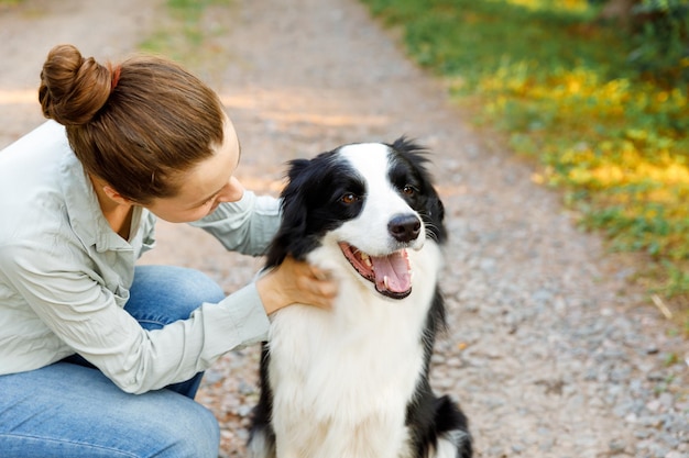 Smiling young attractive woman playing with cute puppy dog border collie on summer outdoor background Girl holding embracing hugging dog friend Pet care and animals concept