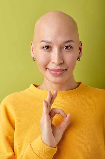 Smiling young bald woman wearing yellow shirt posing isolated on green background