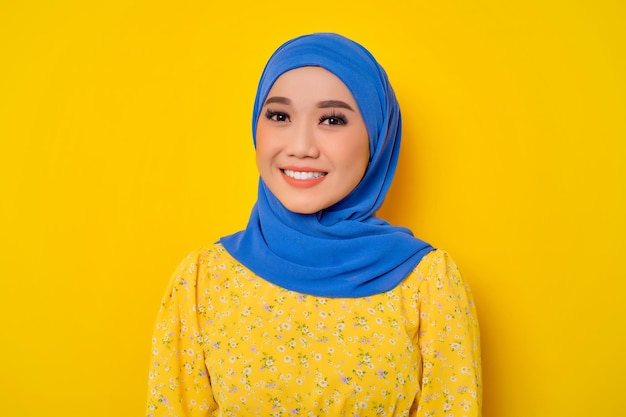 Smiling young beautiful Asian Muslim woman looking at camera isolated over yellow background