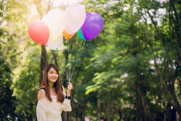 Smiling young beautiful asian women with long brown hair in the park. With rainbow-colored air balloons in her hands.sunny and positive energy of nature.