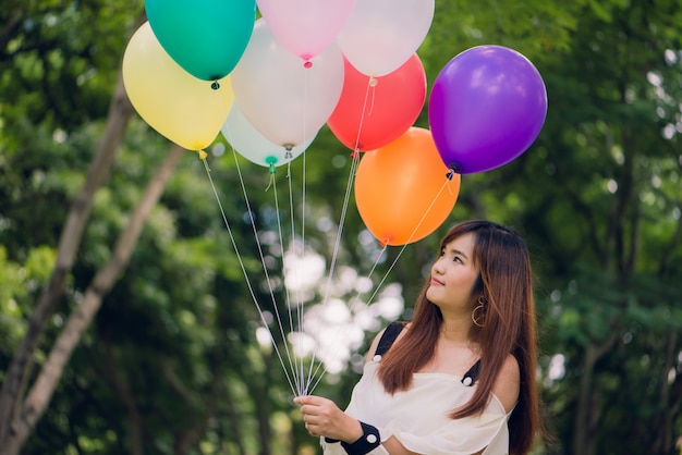 Smiling young beautiful asian women with long brown hair in the park. With rainbow-colored air balloons in her hands.sunny and positive energy of nature.