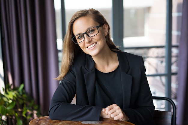 smiling young beautiful brown-haired woman looking at camera and sitting at cafe