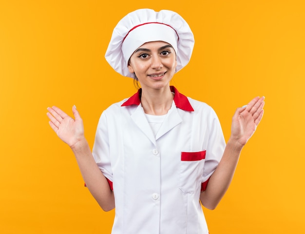 Smiling young beautiful girl in chef uniform spreading hands 