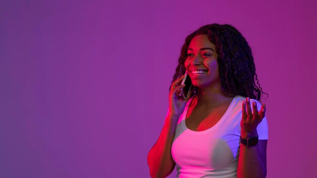 Smiling young black female talking on cellphone in neon light