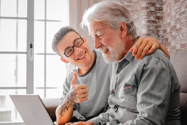 Smiling young boy helping senior grandfather browse with laptop and choose goods or services on web surfing together at home Younger generation caring about older relatives teaching using computer